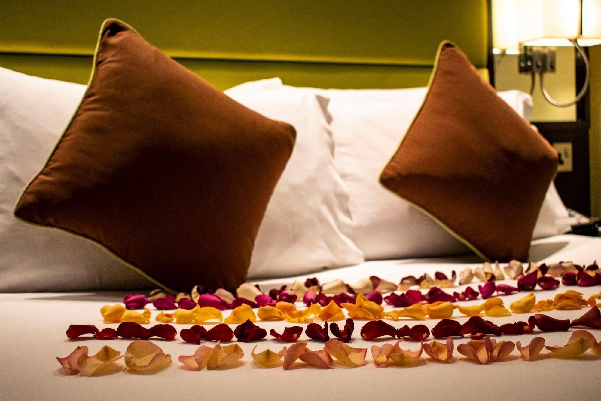 מלון לונדון Montcalm Brewery Townhouse מראה חיצוני תמונה The photo shows a neatly arranged bed with two white pillows and brown decorative cushions. Scattered across the bed is a decorative display of flower petals in various colors, including pink, yellow, and orange, creating a romantic or tranquil ambia