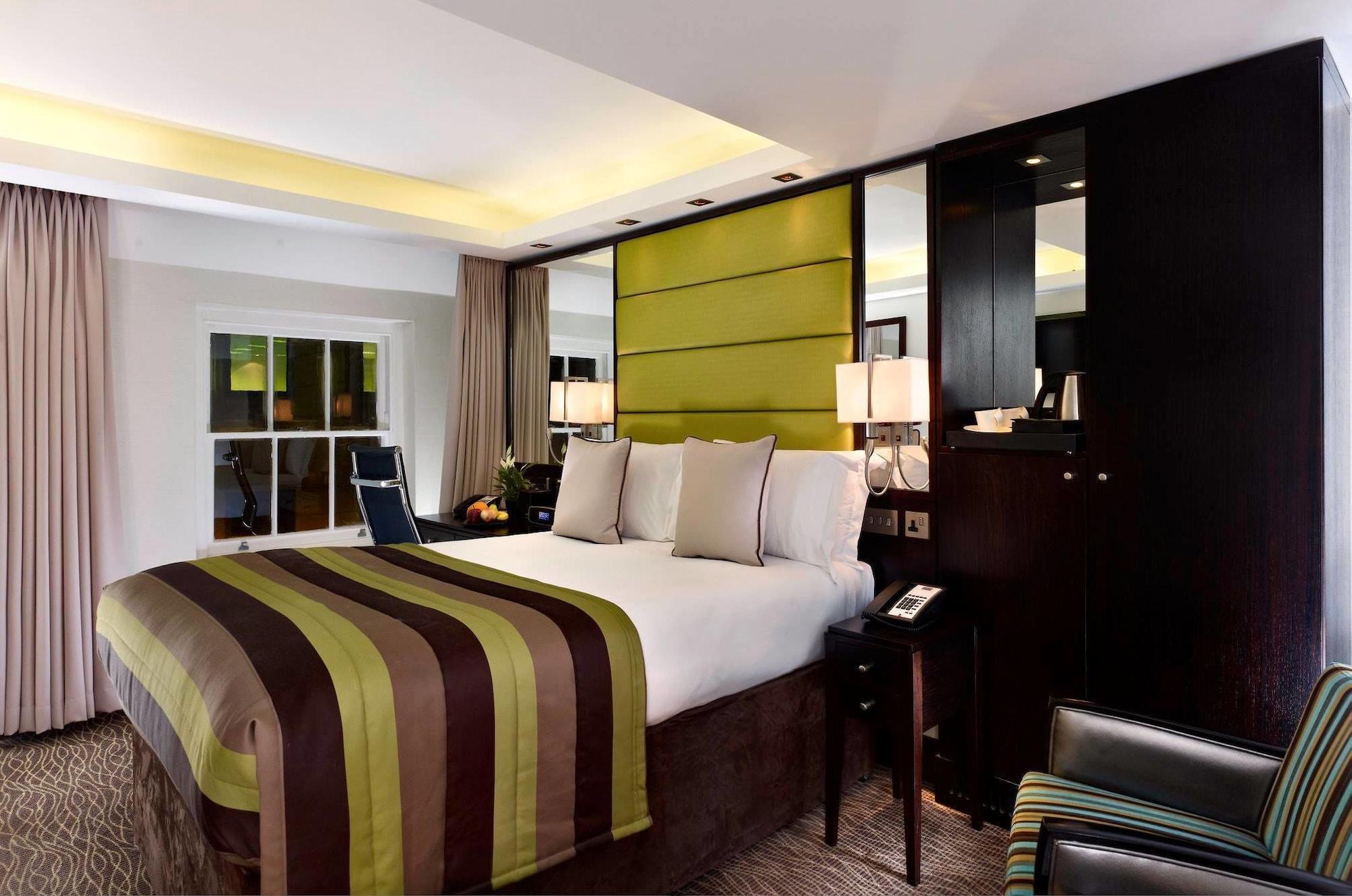 מלון לונדון Montcalm Brewery Townhouse מראה חיצוני תמונה The photo shows a modern hotel room featuring a large bed with a striped comforter in shades of green, brown, and cream. The bed is adorned with several decorative pillows. Behind the bed, there is a contemporary headboard with a green panel design. 