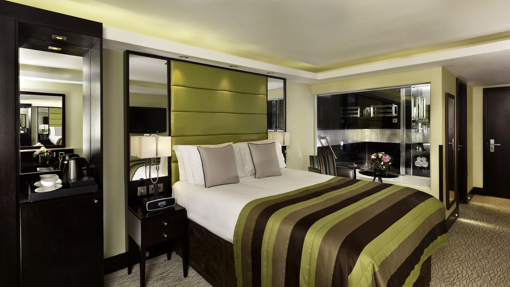 מלון לונדון Montcalm Brewery Townhouse מראה חיצוני תמונה The photo shows a modern hotel room designed with a sophisticated aesthetic. It features a comfortable double bed with a striped brown and green bedspread, complemented by two light gray decorative pillows. Behind the bed is an elegant headboard sect