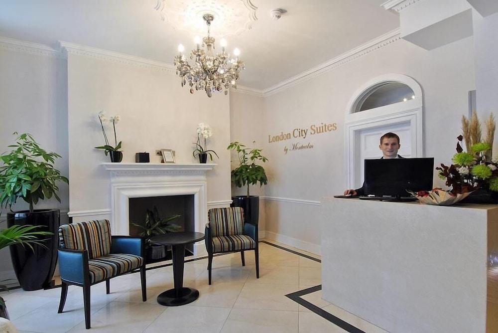 מלון לונדון Montcalm Brewery Townhouse מראה חיצוני תמונה The photo shows the interior of a reception area in a hotel called "London City Suites." The space features a light-colored wall with the hotel's name displayed. There is a stylish chandelier hanging from the ceiling, providing warm lighting. 

In th