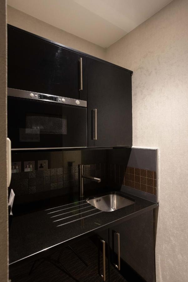 מלון לונדון Montcalm Brewery Townhouse מראה חיצוני תמונה The photo shows a modern kitchen setup with a dark color scheme. It features:

- A built-in microwave oven situated above a countertop.
- A sleek black cabinet beneath the microwave, which likely stores kitchen items.
- A stainless steel sink placed 