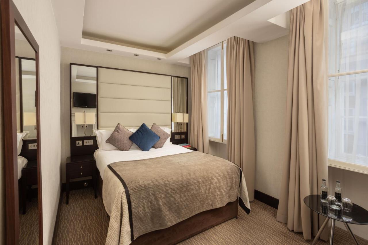 מלון לונדון Montcalm Brewery Townhouse מראה חיצוני תמונה The photo shows a cozy hotel bedroom. The room features a neatly made double bed with a beige bedspread and decorative pillows, including a blue one. There are bedside tables on either side of the bed with lamps. The walls are painted in a soft color