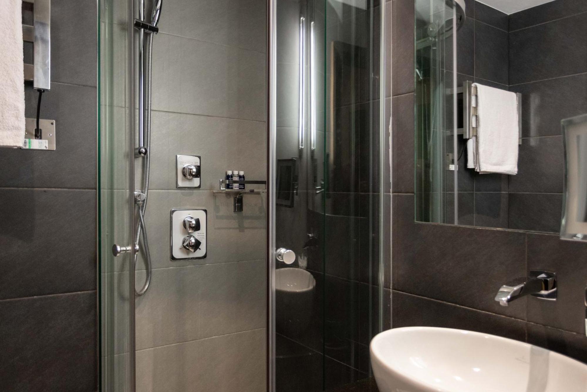 מלון לונדון Montcalm Brewery Townhouse מראה חיצוני תמונה The photo shows a modern bathroom with a glass shower enclosure. The shower features a handheld showerhead and various controls mounted on the wall. The walls are tiled in dark, sleek tones, contributing to a contemporary aesthetic. There is a round 