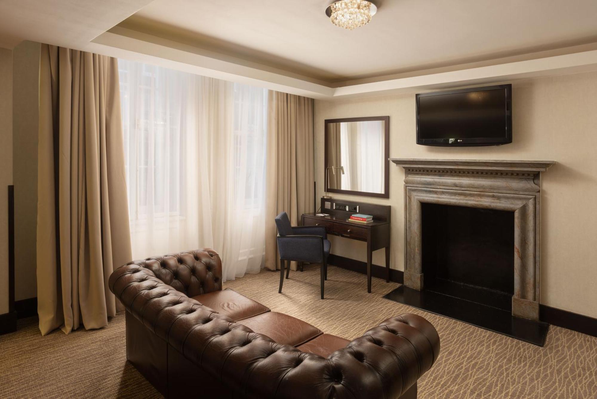 מלון לונדון Montcalm Brewery Townhouse מראה חיצוני תמונה The photo shows a stylish interior of a room, likely a living area or a hotel suite. It features a dark leather chesterfield sofa with tufted upholstery. Opposite the sofa is a small wooden desk with a chair, positioned near a wall-mounted flat-scree