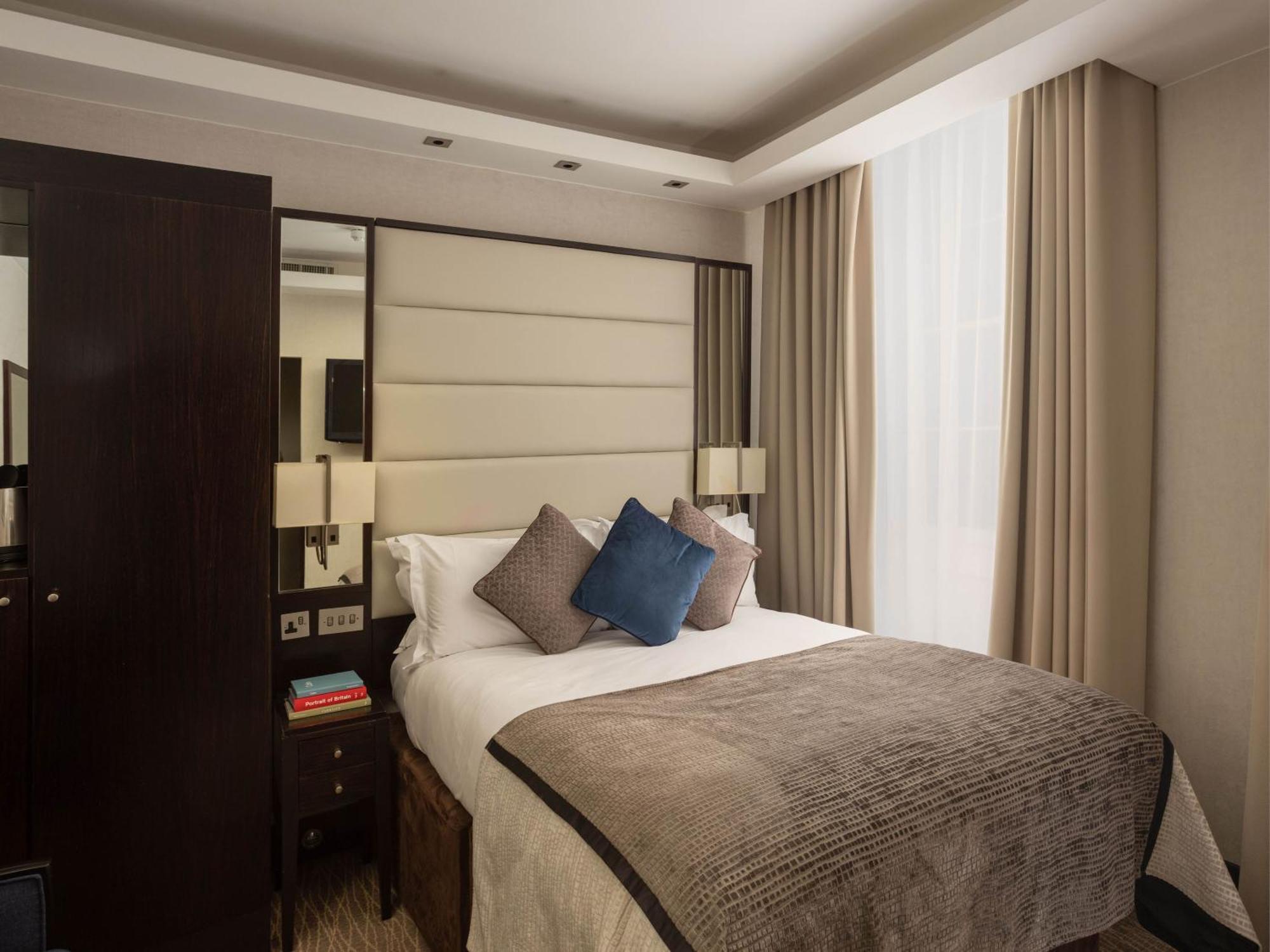 מלון לונדון Montcalm Brewery Townhouse מראה חיצוני תמונה The image shows a cozy bedroom. It features a comfortable double bed with a light-colored duvet and decorative pillows in shades of blue and gray. The headboard is upholstered in a soft material, and there are bedside lamps on either side of the bed.