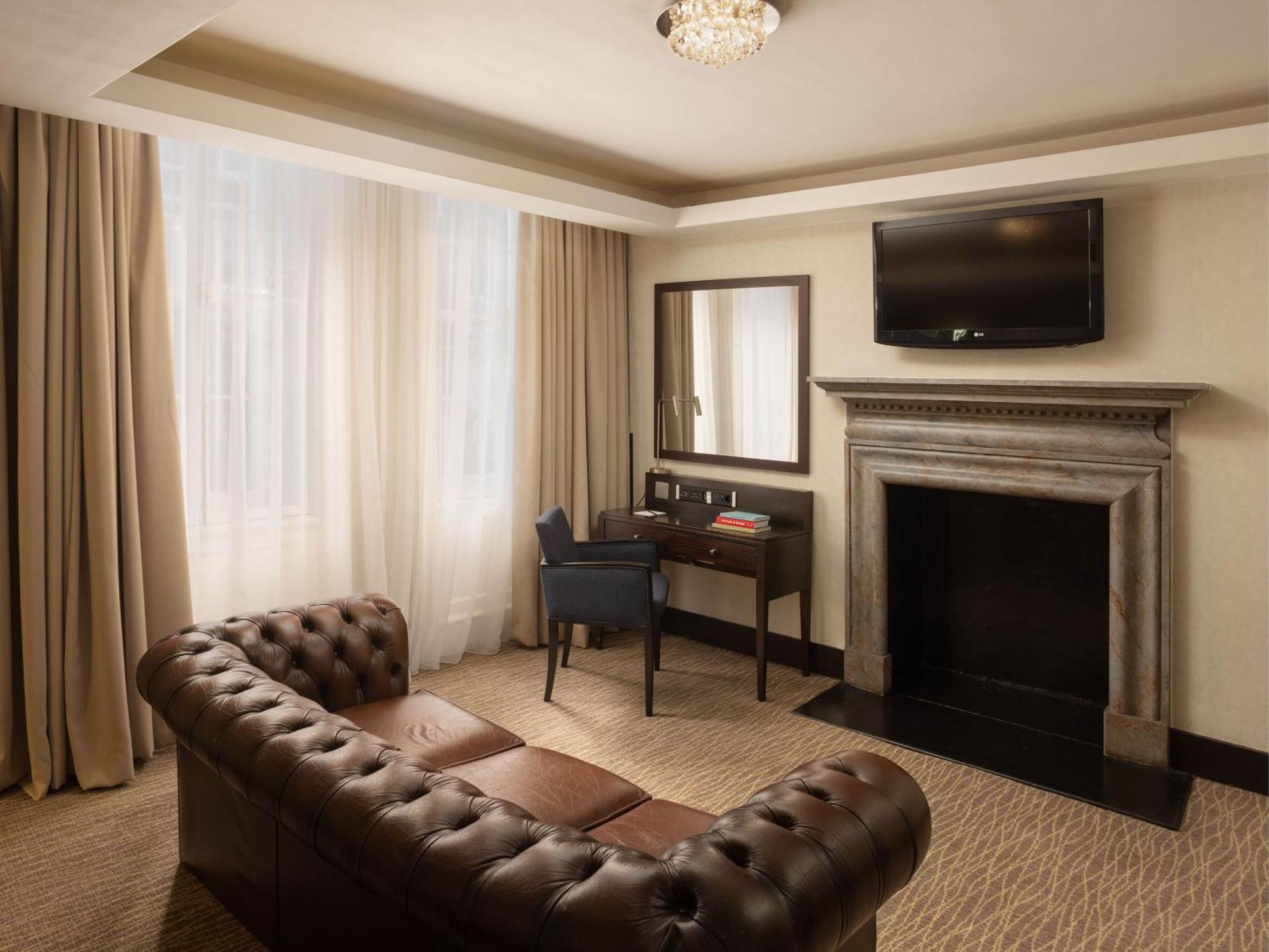 מלון לונדון Montcalm Brewery Townhouse מראה חיצוני תמונה The photo shows a cozy and elegantly designed room. There is a comfortable brown leather sofa with tufted detailing. A small desk and chair are positioned near a mirror, providing a space for work or personal grooming. On the wall, a flat-screen TV i