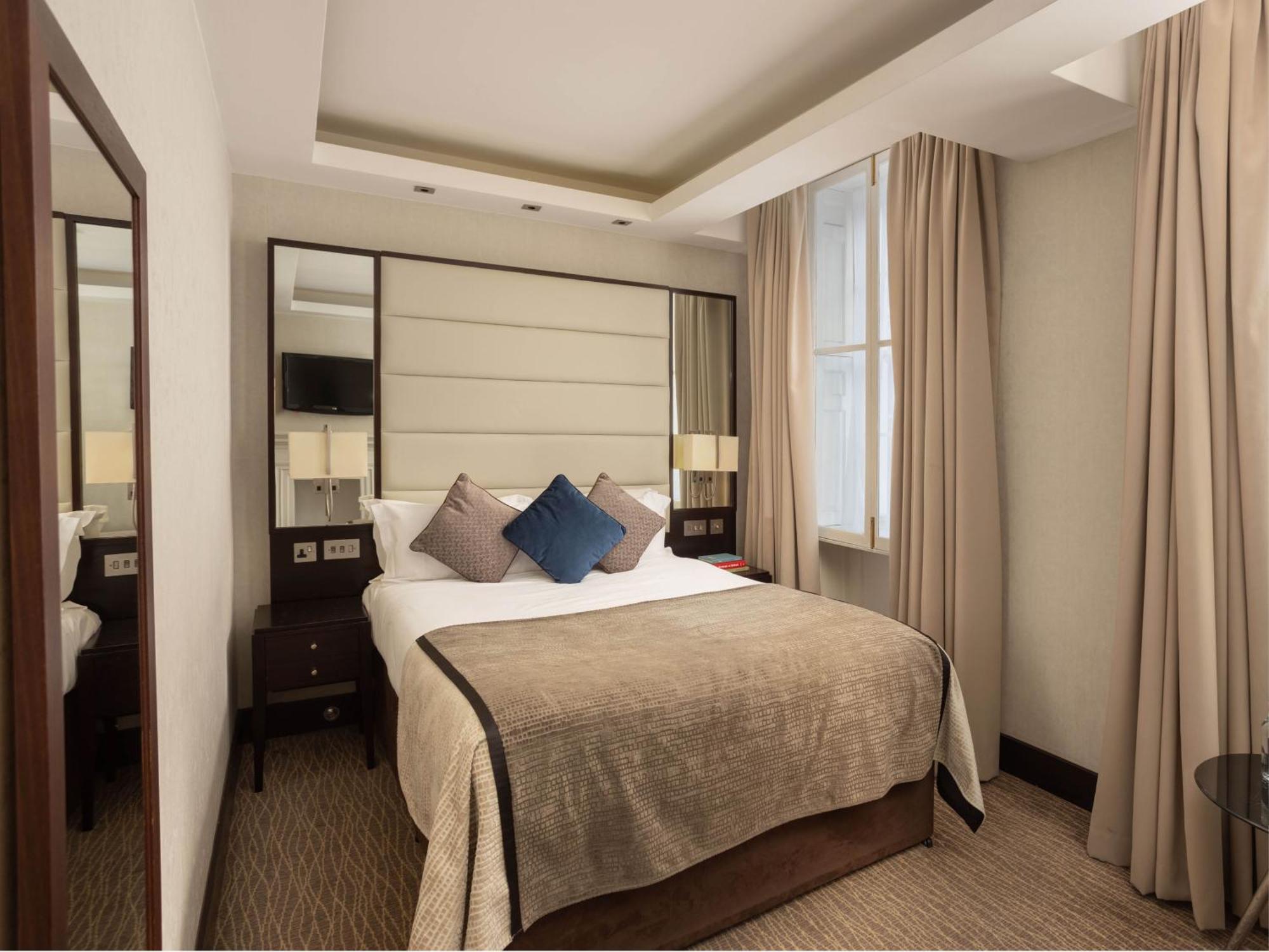 מלון לונדון Montcalm Brewery Townhouse מראה חיצוני תמונה The photo shows a cozy hotel room with a bed as the focal point. The bed is made with neutral-colored linens and has several pillows, including a decorative blue one. There are bedside tables on either side of the bed, each with a lamp. A large mirro