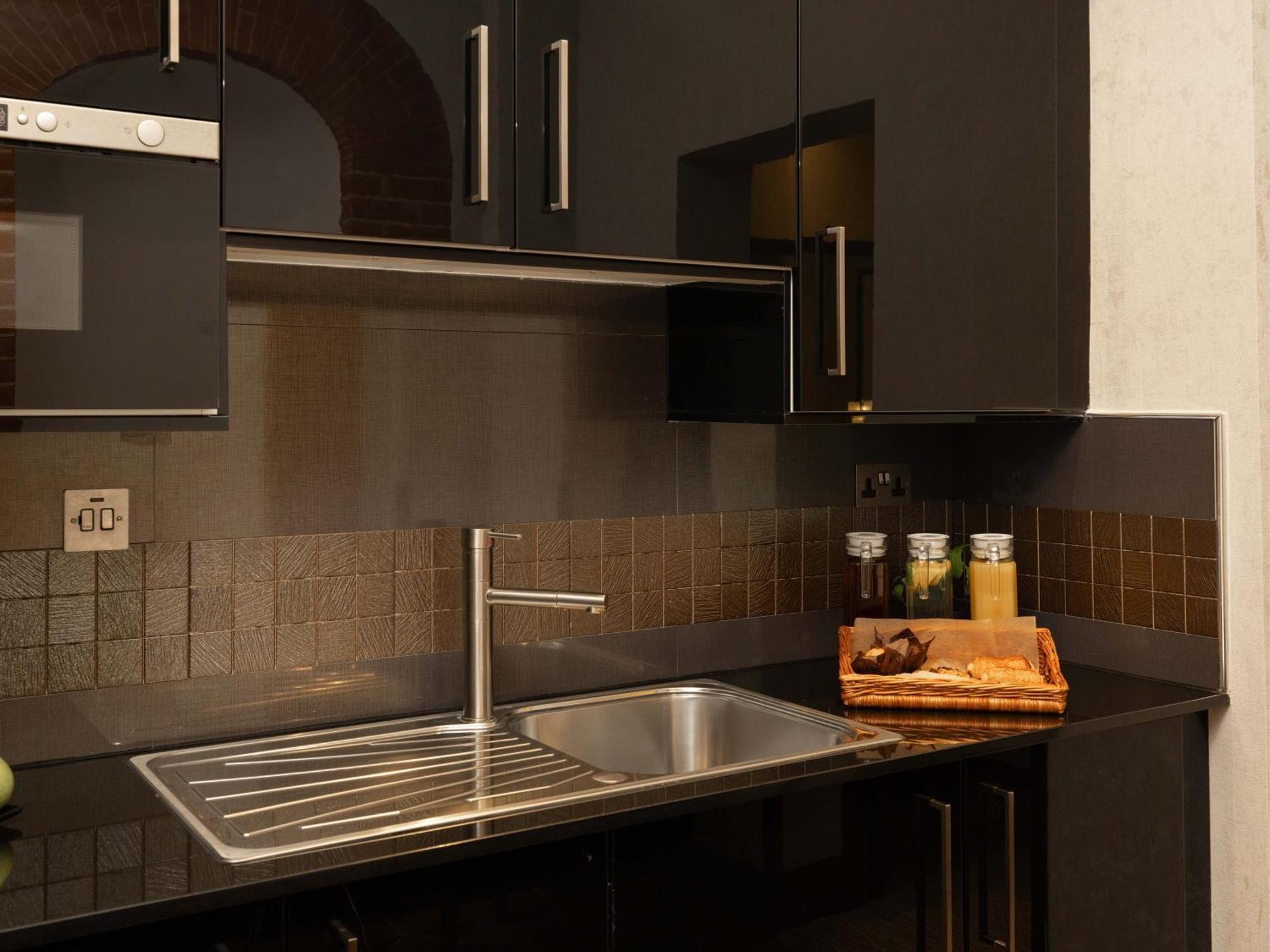 מלון לונדון Montcalm Brewery Townhouse מראה חיצוני תמונה The photo shows a modern kitchen with a sleek design. It features dark cabinetry with a glossy finish and stainless steel handles. There is a stainless steel sink with a simple faucet, and a countertop made of black material. Above the sink, there ar