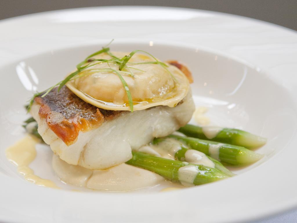 מלון לונדון Montcalm Brewery Townhouse מראה חיצוני תמונה The image shows a beautifully presented dish featuring a piece of fish, likely a white fish, topped with a clam. It is served on a bed of green asparagus spears. The dish is garnished with thinly sliced herbs or greens, adding a touch of color. The s