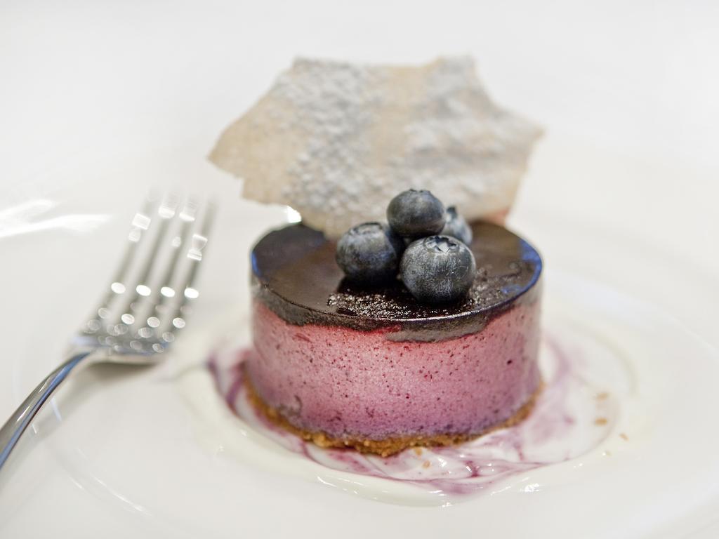 מלון לונדון Montcalm Brewery Townhouse מראה חיצוני תמונה The photo shows a beautifully plated dessert, which appears to be a round cheesecake or mousse. It has a pinkish-purple filling, topped with a glossy dark chocolate layer. Three fresh blueberries sit on top, adding a pop of color. The dessert is acco
