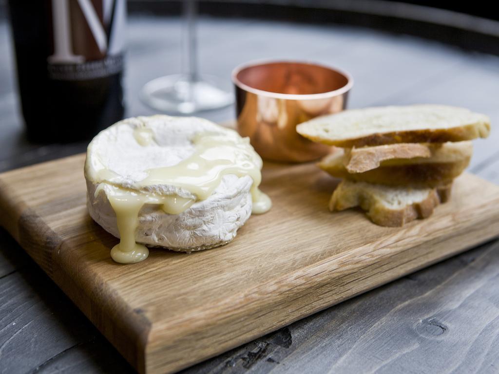 מלון לונדון Montcalm Brewery Townhouse מראה חיצוני תמונה The photo features a wooden serving board with several items. There is a round cheese, likely Brie or a similar soft cheese, that appears to be melting and dripping slightly. Next to the cheese, there is a small copper cup that might contain a sauce 