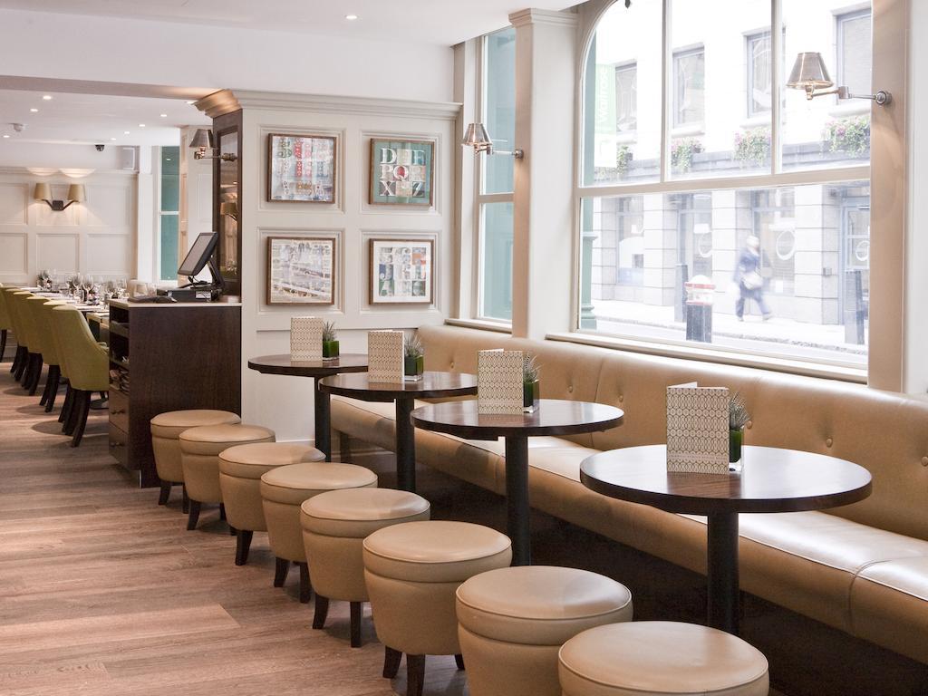 מלון לונדון Montcalm Brewery Townhouse מראה חיצוני תמונה The photo displays a modern café or restaurant interior. There is a cozy seating area featuring light-colored, upholstered benches along the wall, accompanied by small round tables. The tables are paired with circular stools. The decor includes frame