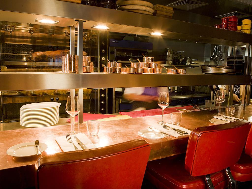 מלון לונדון Montcalm Brewery Townhouse מראה חיצוני תמונה The photo shows a restaurant interior featuring a bar or counter area. There are red chairs arranged around a copper-topped table where dining utensils and plates are set. Above the counter, there are shelves displaying various cooking pots and kitch