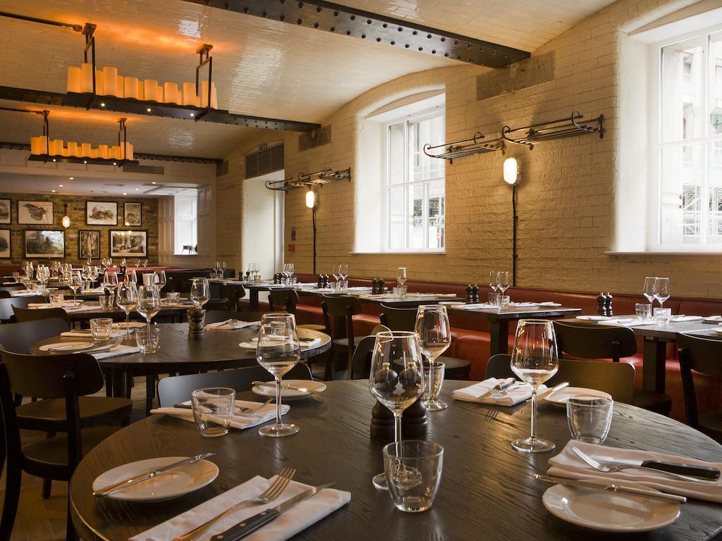 מלון לונדון Montcalm Brewery Townhouse מראה חיצוני תמונה The photo shows a restaurant interior featuring a warm and inviting atmosphere. It has several round wooden tables set for dining, each with neatly arranged plates, utensils, and glasses. The lighting is soft, with overhead fixtures providing a cozy 