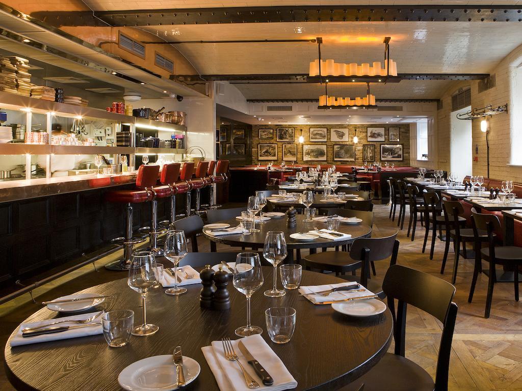 מלון לונדון Montcalm Brewery Townhouse מראה חיצוני תמונה The photo shows the interior of a stylish restaurant. It features several round tables set with white plates, glasses, and silverware, all neatly arranged for dining. The decor includes a modern design with wooden floors and a mix of lighting fixture
