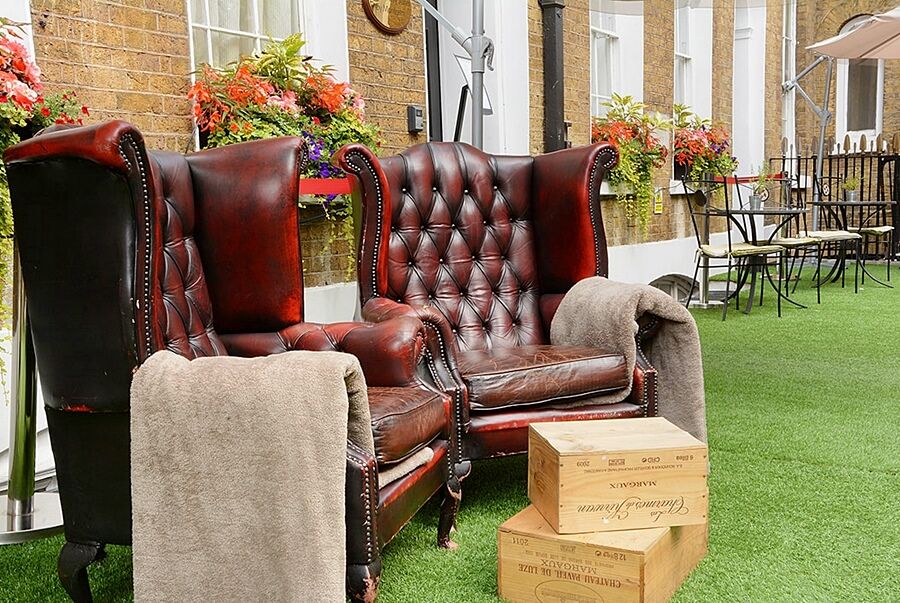 מלון לונדון Montcalm Brewery Townhouse מראה חיצוני תמונה The photo depicts two large, elegant armchairs with a classic design, featuring rich burgundy leather upholstery and button tufting. They are positioned in a cozy outdoor setting, with lush green artificial grass beneath them. Next to the chairs, the