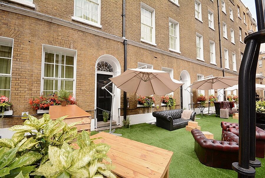 מלון לונדון Montcalm Brewery Townhouse מראה חיצוני תמונה The photo depicts an outdoor area of a building with a brick facade. There are several large windows visible, along with a wooden door. The setting features outdoor furniture, including couches in a dark leather finish and wooden tables. Large umbrel